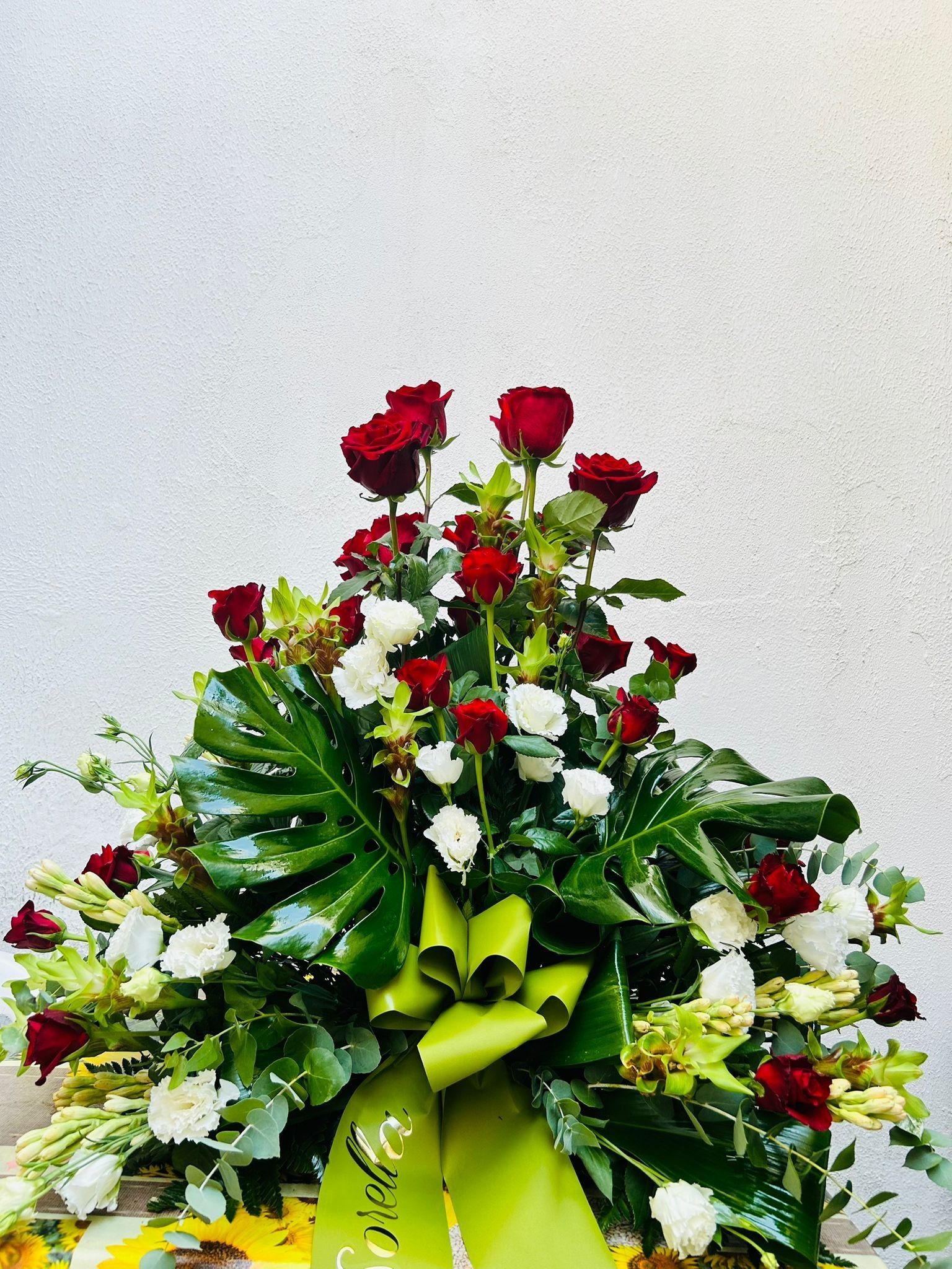 Rose rosse e bianche in una composizione floreale con un nastro verde su sfondo bianco.