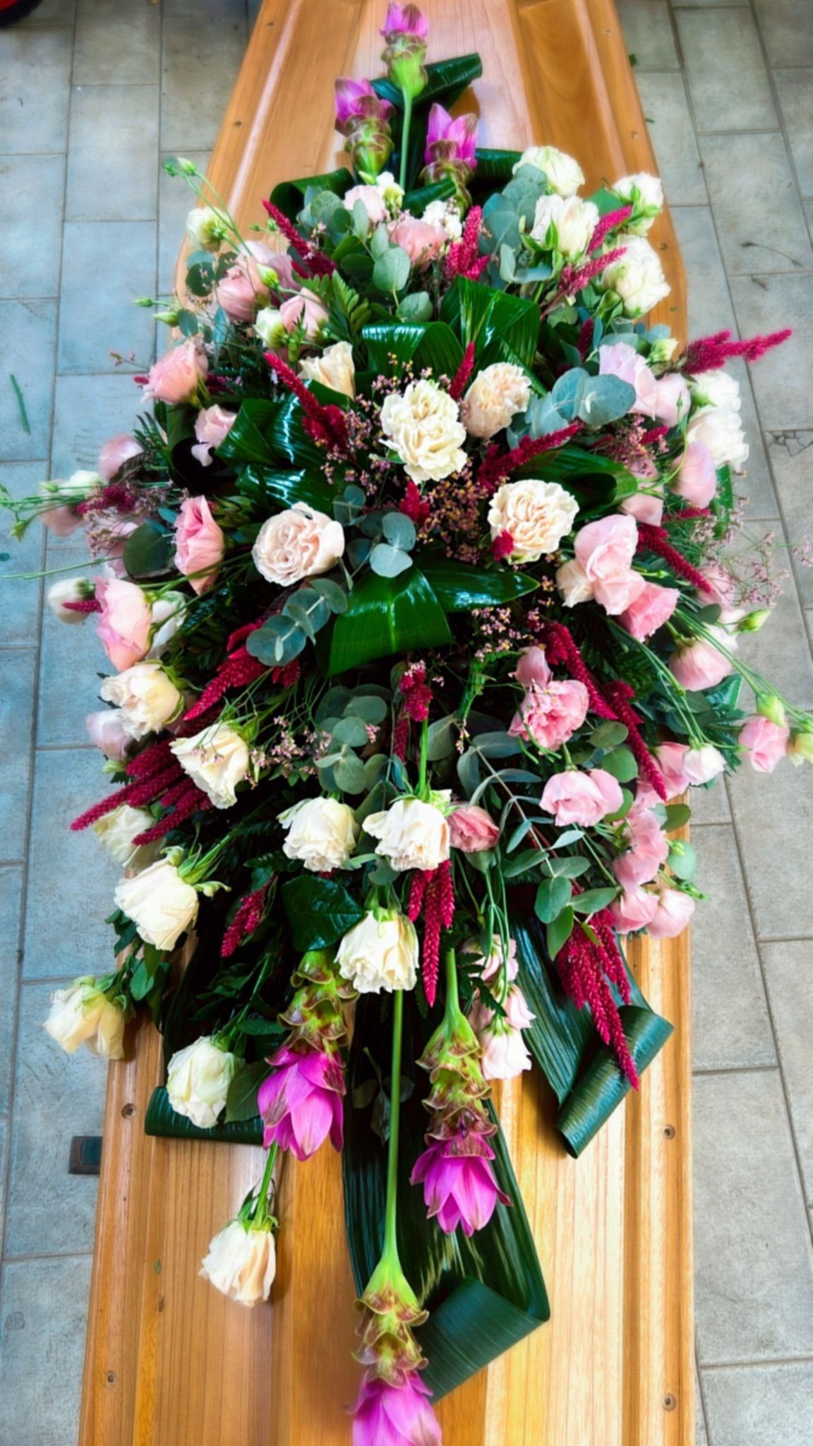 Composizione floreale di fiori rosa, crema e rossi che ricadono a cascata su una bara di legno.