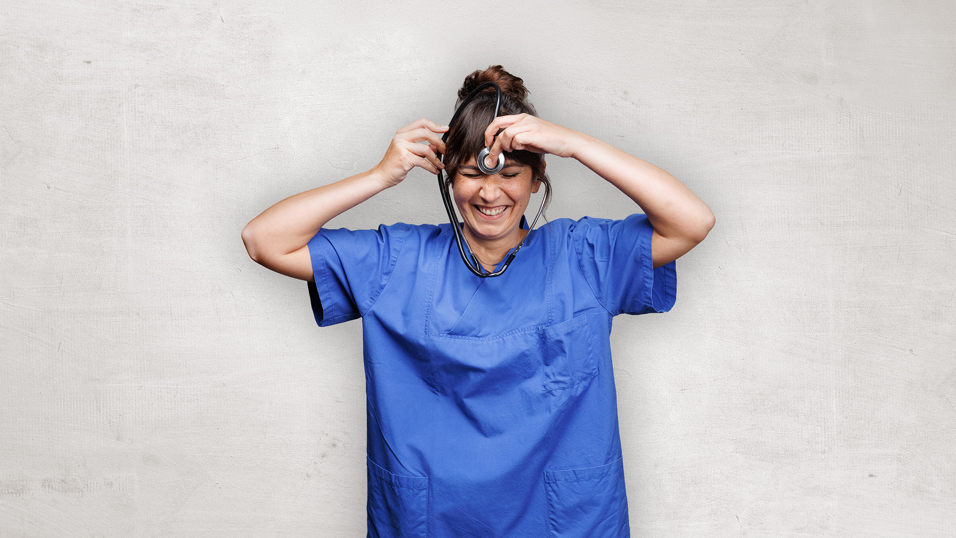 Eine Person in blauer OP-Kleidung zupft sich an den Haaren vor einer schlichten Wand und sieht gestresst aus.