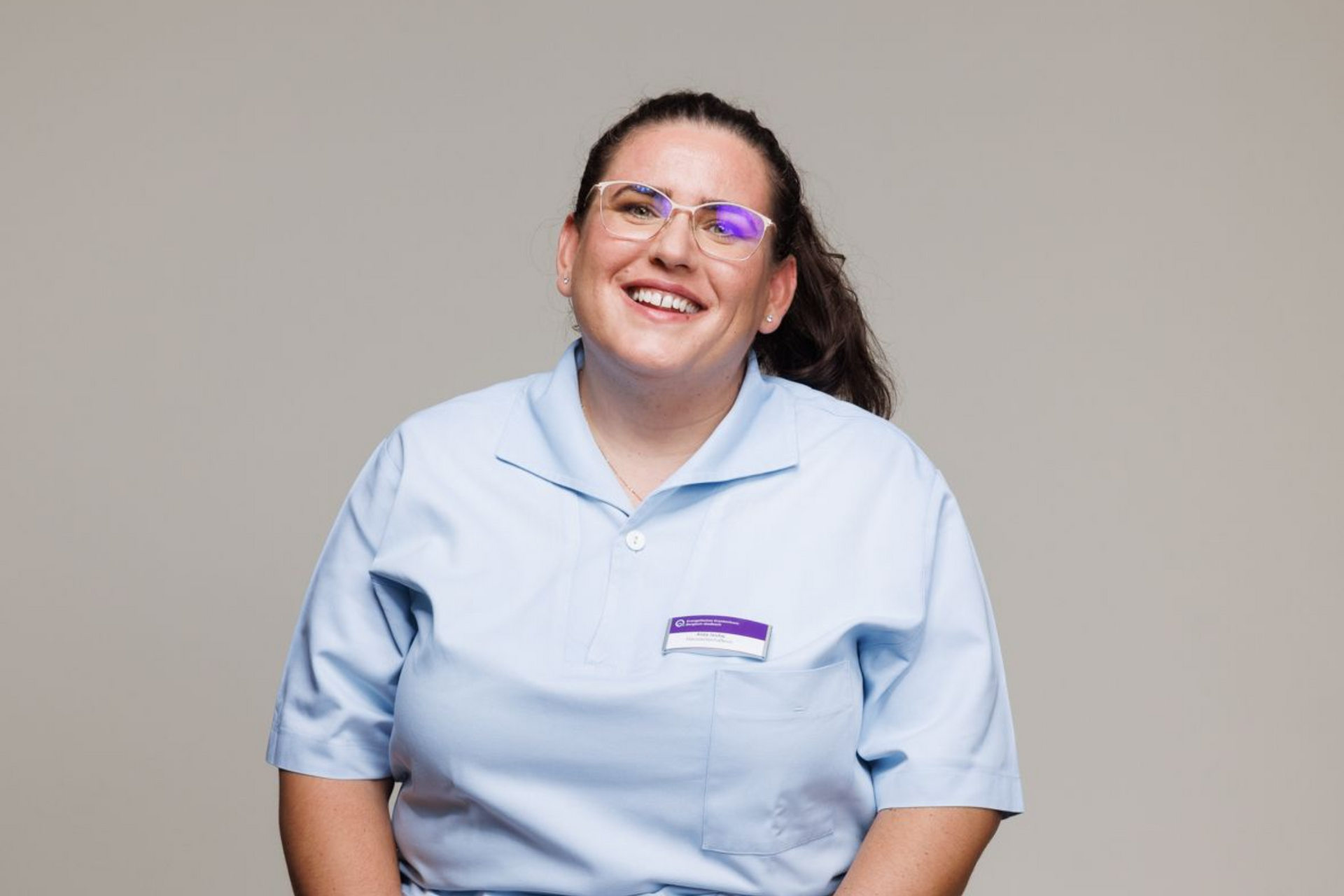 Lächelnde Person in einem hellblauen Uniformhemd vor einfarbig grauem Hintergrund