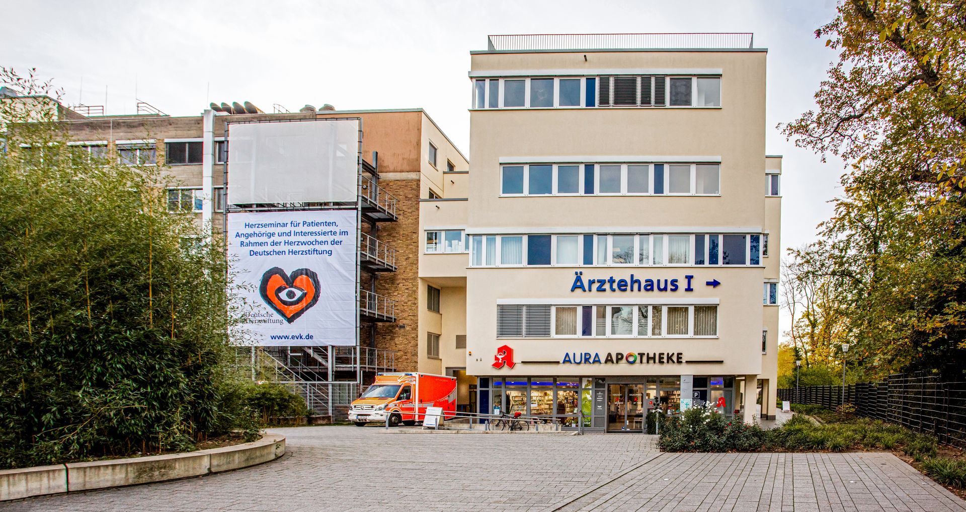 Modernes Ärztehaus im Eingangsbereich des Evanglischen Krankenhauses Bergisch Gladbach. Darunter eine Apotheke auf einem geflasterten Boden.