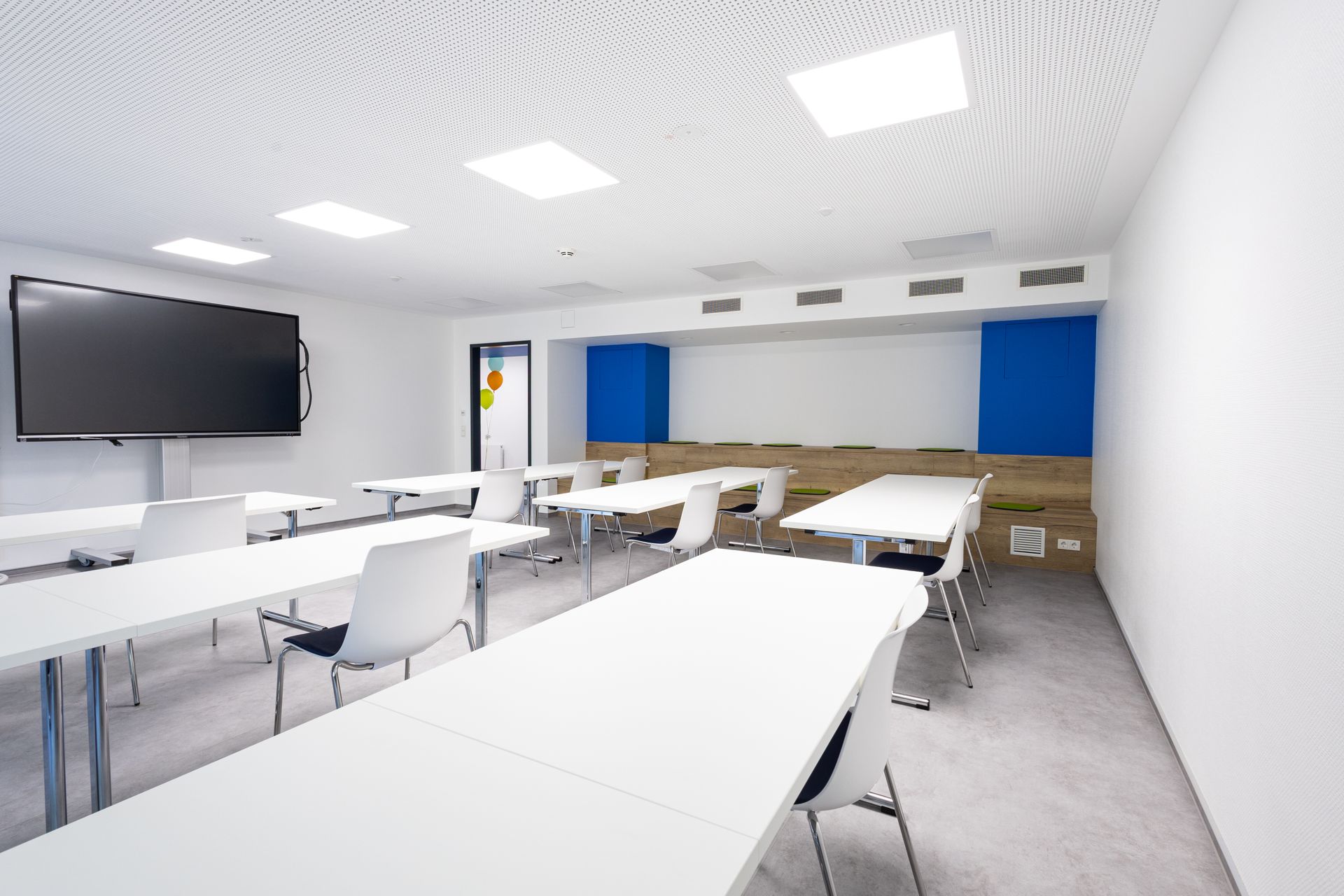 Modernes Klassenzimmer der Quirlsberg Akademie. Weiße Tische und Stühle mit Sitzgelegenheiten an der Wand.