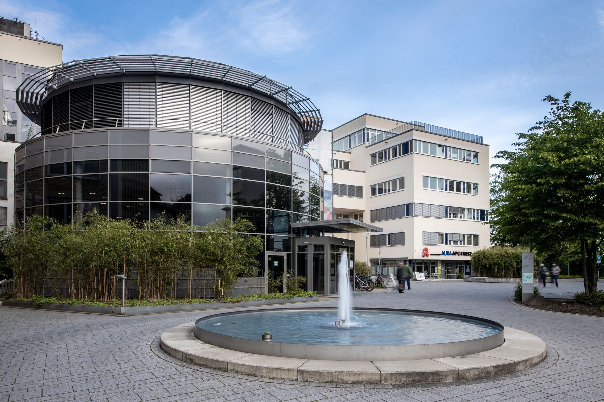 Eingangsbereich des Gesundheitscampus Quirlsberg in Bergisch Gladbach mit dem Evangelischen Krankenhaus und angrenzenden Gebäuden. Ein moderner Brunnen im Vordergrund.