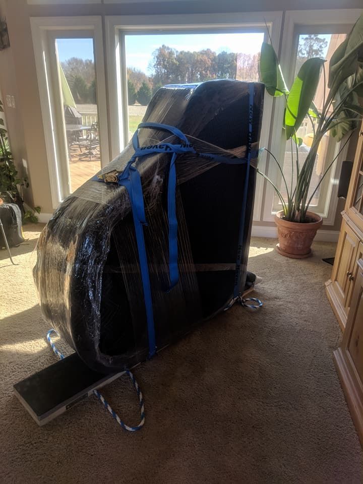 A piano is wrapped in plastic and being moved in a living room.