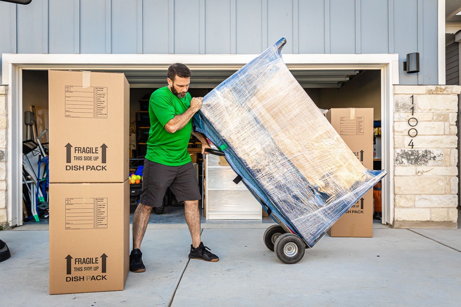 A man is pushing a cart with a table on it in front of a garage.