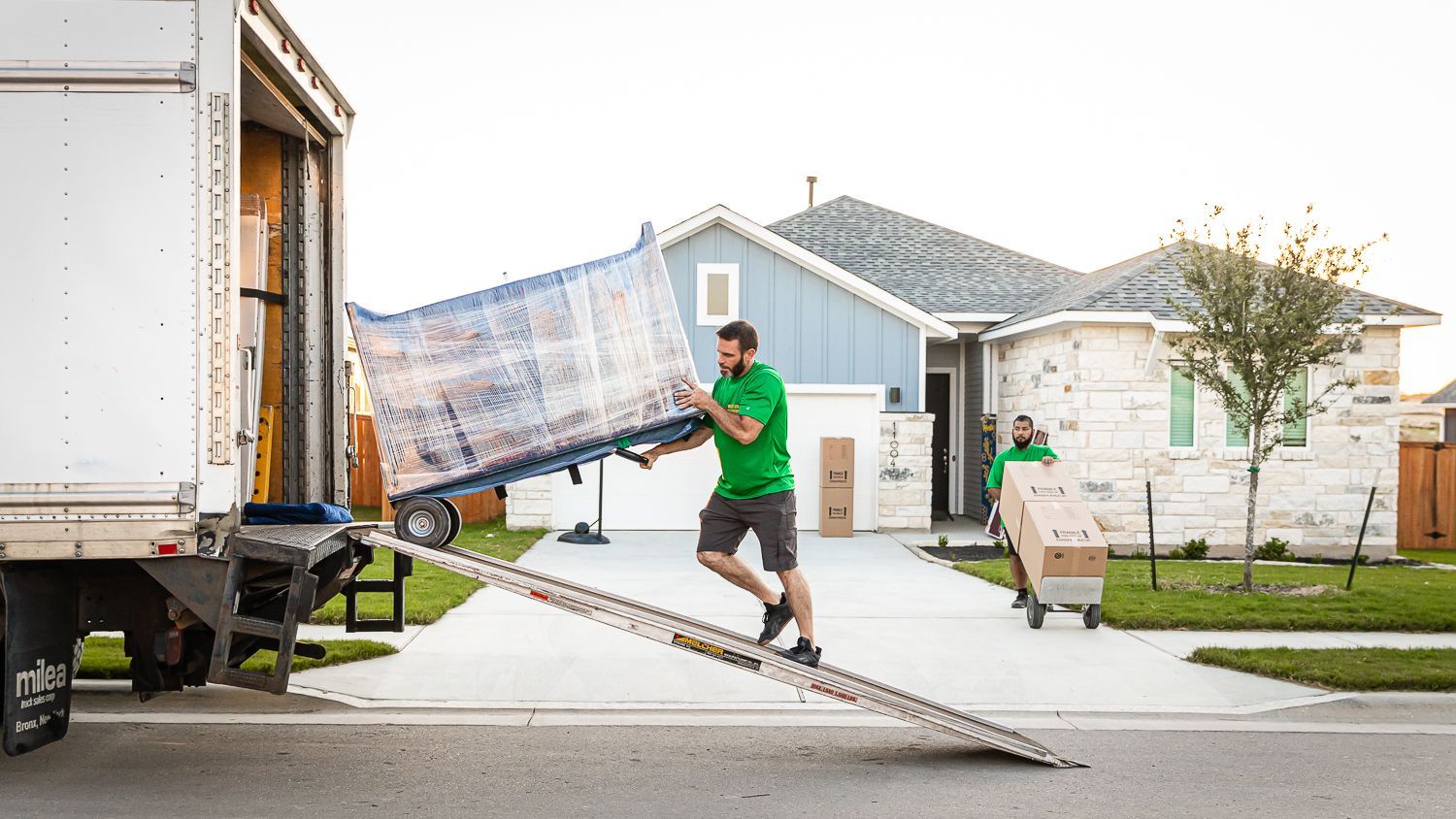 A man is carrying a couch on a ramp towards a moving truck.