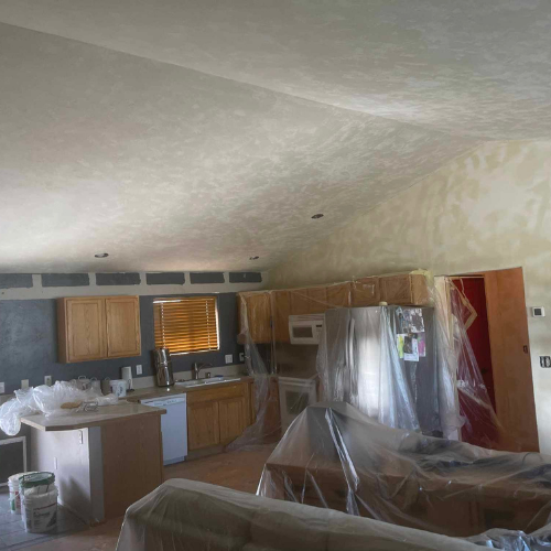 Kitchen undergoing renovation, cabinets covered, appliances protected with plastic sheeting.