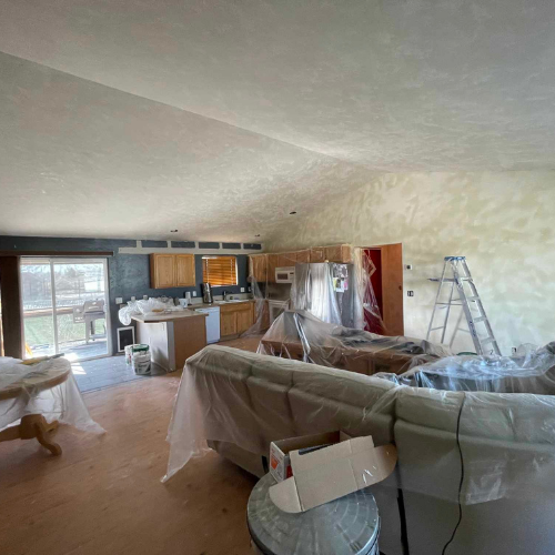 Interior room under renovation, with plastic covering furniture, ladder, and partially painted walls.