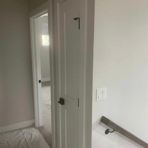 White interior doors in hallway, one open to a room. Light switch and stair rail visible.