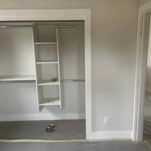 A walk-in closet with shelves, hanging rods, and grey carpet. White trim and walls, with an adjacent doorway.