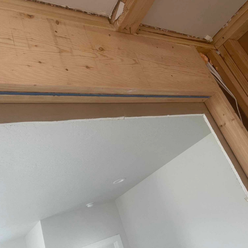 Wooden frame with drywall, doorway opening to a white-walled room, and exposed beams.