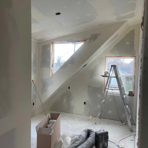 Interior room under construction with drywall and a ladder by a window.