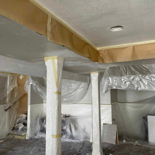 Interior space prepared for painting: columns, ceiling, and trim covered with plastic and paper.