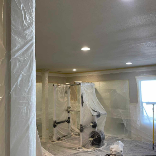 Room being painted, covered in plastic sheeting. Weight machine visible.