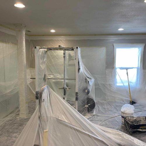 Room under renovation, covered in plastic sheeting. A weight rack and window visible.