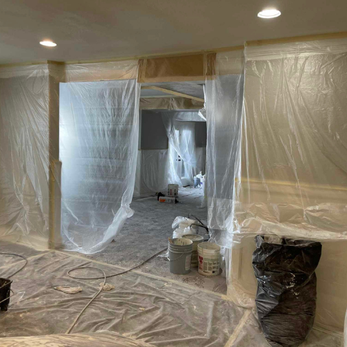 Interior room covered in plastic sheeting for painting. Buckets and tools on the floor.
