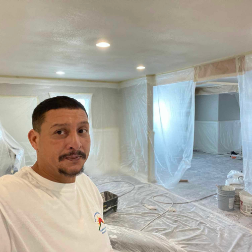 Man in white shirt in a room covered in plastic sheeting, preparing for painting.