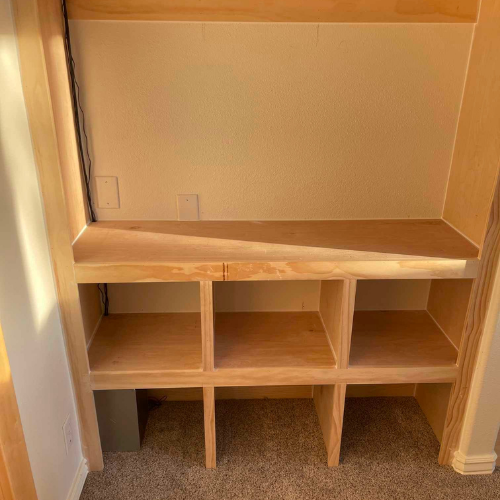 Built-in wooden storage unit with shelves and cubbies inside a closet, neutral colors.
