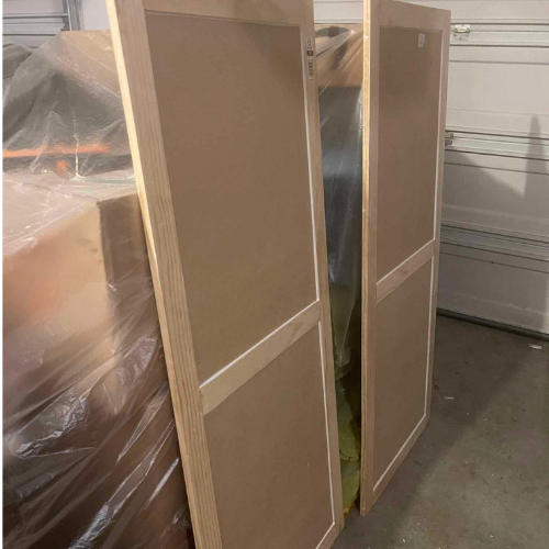 Two unfinished wood doors with tan panels. Inside a garage.
