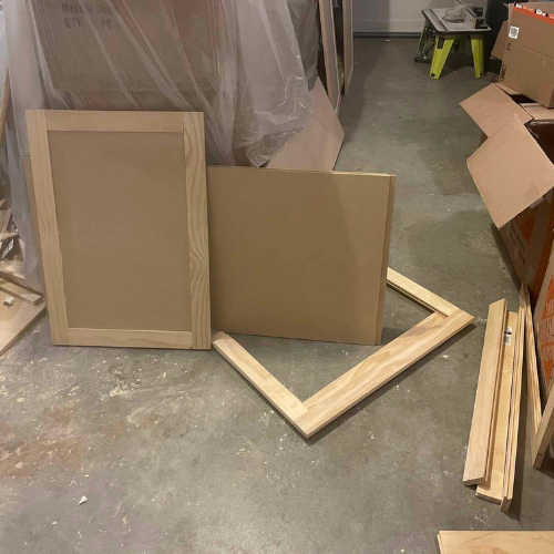 Cabinet doors and frame pieces on a concrete floor in a workshop setting.