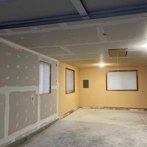 Garage interior with drywall on walls and ceiling; windows, electrical panel, and concrete floor.