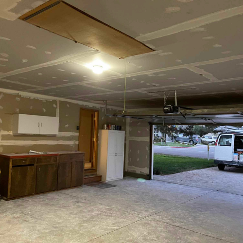 Garage interior with exposed ceiling hatch, cabinets, and open garage door.