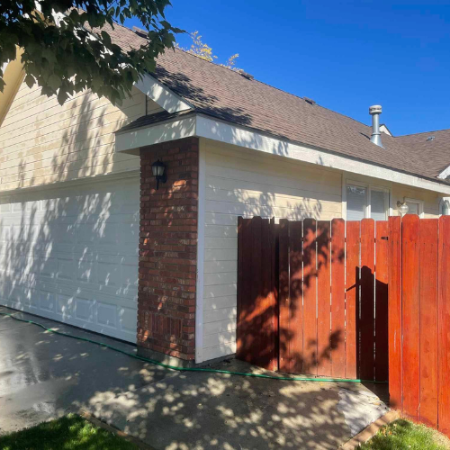 Garage with white door, brick pillar, and brown fence against a sunny sky.