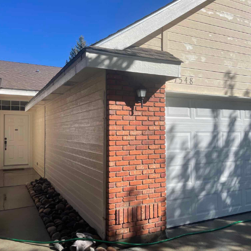 Exterior view of a house with beige siding, a brick column, and a white garage door, under a blue sky.