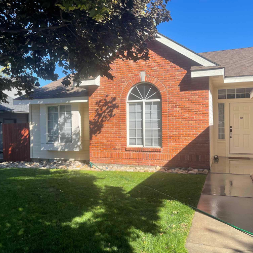 Brick house with arched window, white trim, green lawn, tree shade, and blue sky.