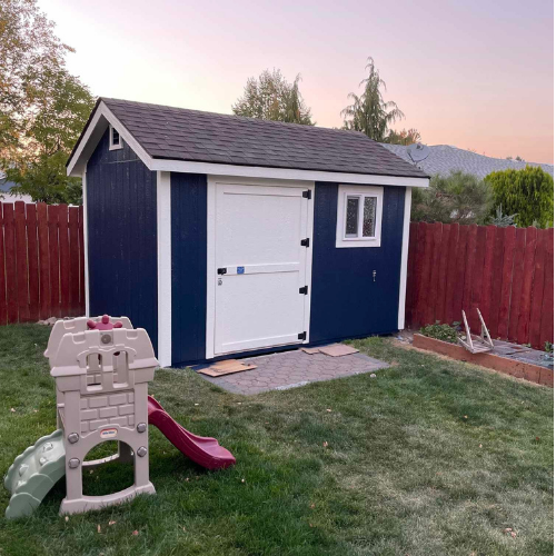 Blue shed with white door and window in a backyard; a child's slide nearby.