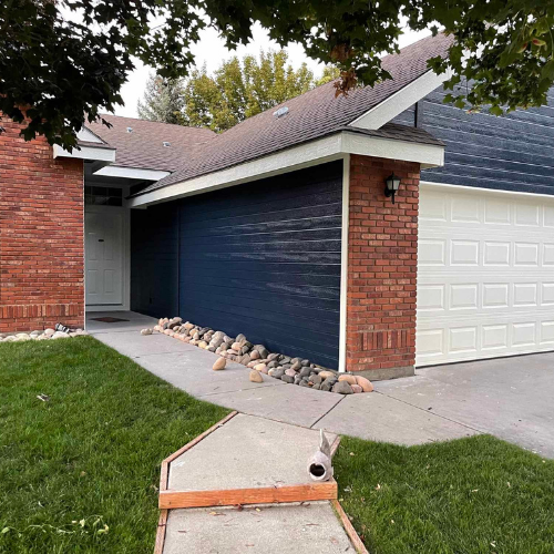 A house exterior with brick, dark blue siding, white garage door, and a concrete path.