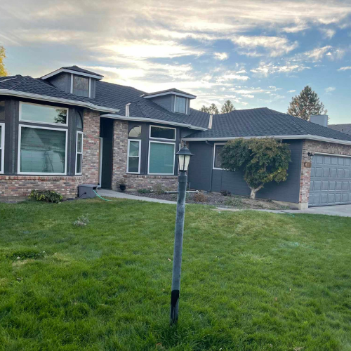 Dark gray house with brick accents, garage, and green lawn under a cloudy sky.