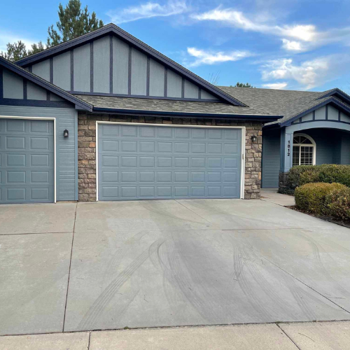 Blue house with a two-car garage, stone accents, and a concrete driveway on a sunny day.