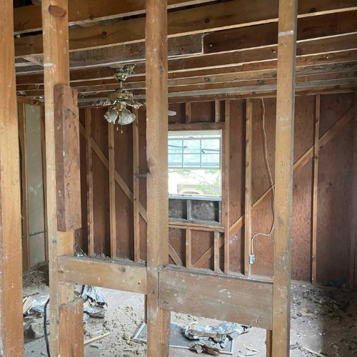 Interior of a room under construction, with exposed wooden studs, a window, and a ceiling fan.