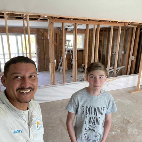Man and boy smiling in a room under renovation with exposed wall framing.