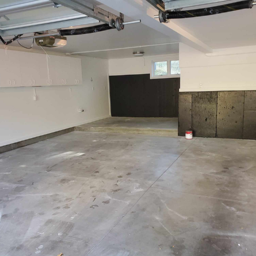 Empty garage with gray concrete floor, white walls, and a section of black wall panels.