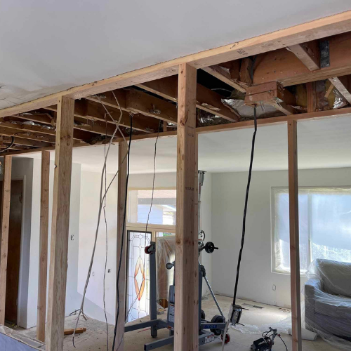 Interior room undergoing renovation, exposed wood frame construction. Electrical wires hang down.