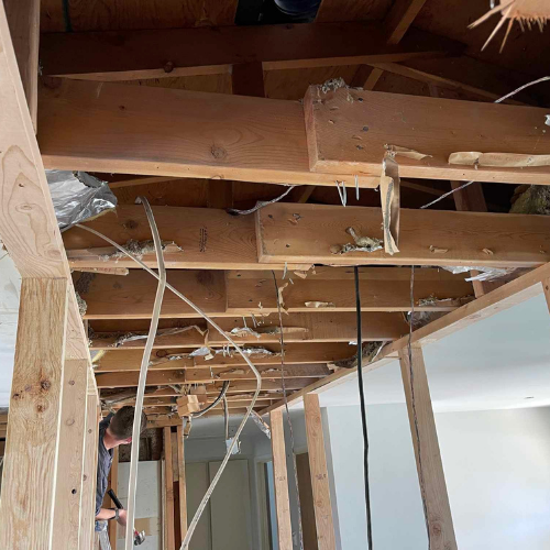 Ceiling and walls under construction; exposed wood beams, electrical wires, and a person working.
