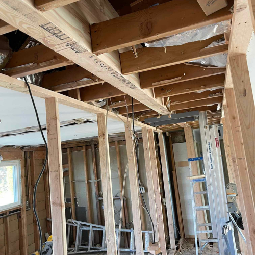 Interior of a room under construction, with exposed wooden beams, studs, and wiring.