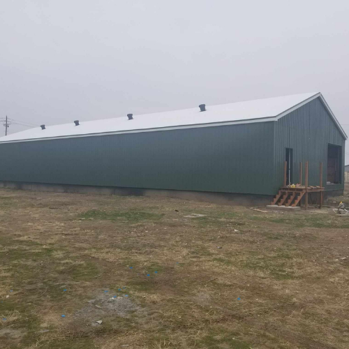 Green metal building with white roof; set in a grassy field on a cloudy day.