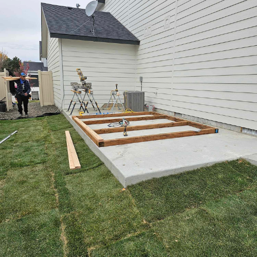 Construction of a wooden frame on a concrete patio next to a house with a person standing nearby.