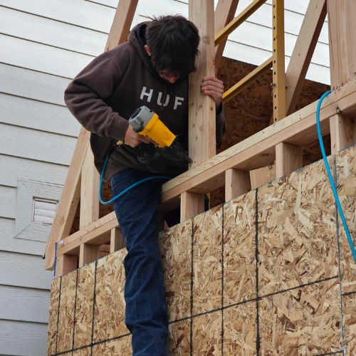 Person in hoodie using nail gun on wooden construction.