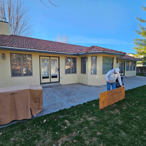 A person placing a board on the lawn in front of a house with a terracotta roof.