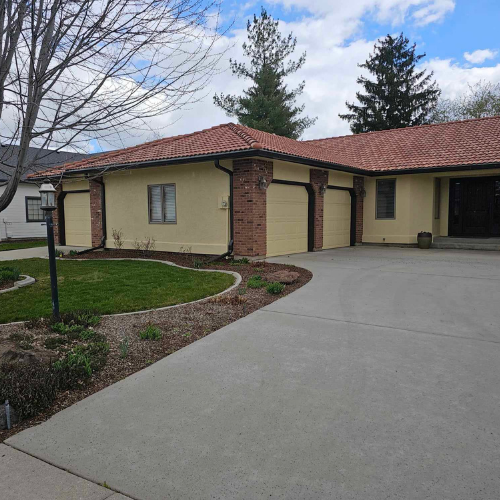 Yellow house with red tile roof, brick accents, and a concrete driveway.