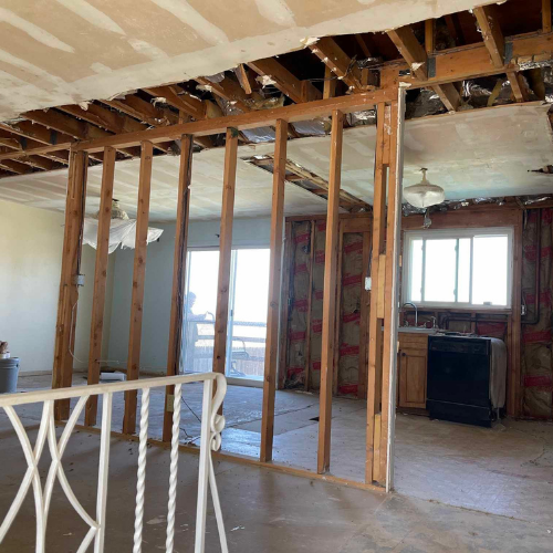 Interior of a house undergoing renovation, with exposed framing, torn walls, and a view to the outside.