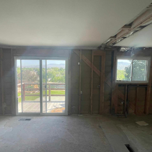 Interior of a room undergoing renovation; exposed wall studs, sliding glass door, window.