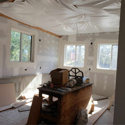 Interior room under construction, with drywall and plastic sheeting on the ceiling.