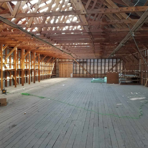 Interior of a large wooden building undergoing renovation, showing exposed beams, wooden floor and unfinished walls.