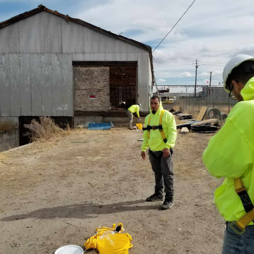 Three construction workers in safety vests and hard hats near a weathered building with an open doorway.