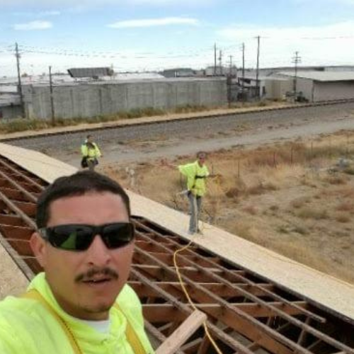Construction workers on rooftop with safety harnesses. One takes selfie. Industrial setting.